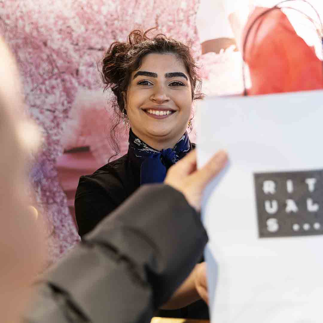 Smiling employee from Rituals gives a customer a bag.